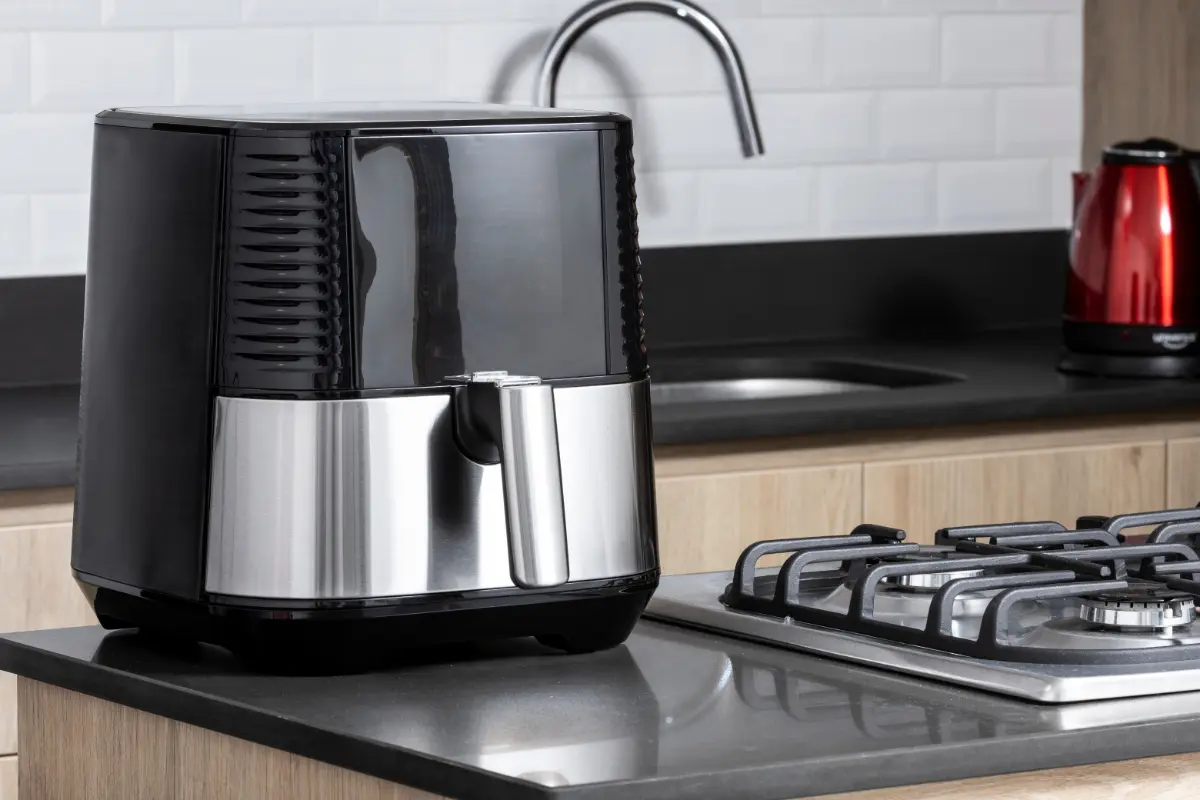 A modern air fryer on a kitchen counter beside a gas stove and a red kettle, set against a subway tile backsplash, embodying contemporary kitchen design.