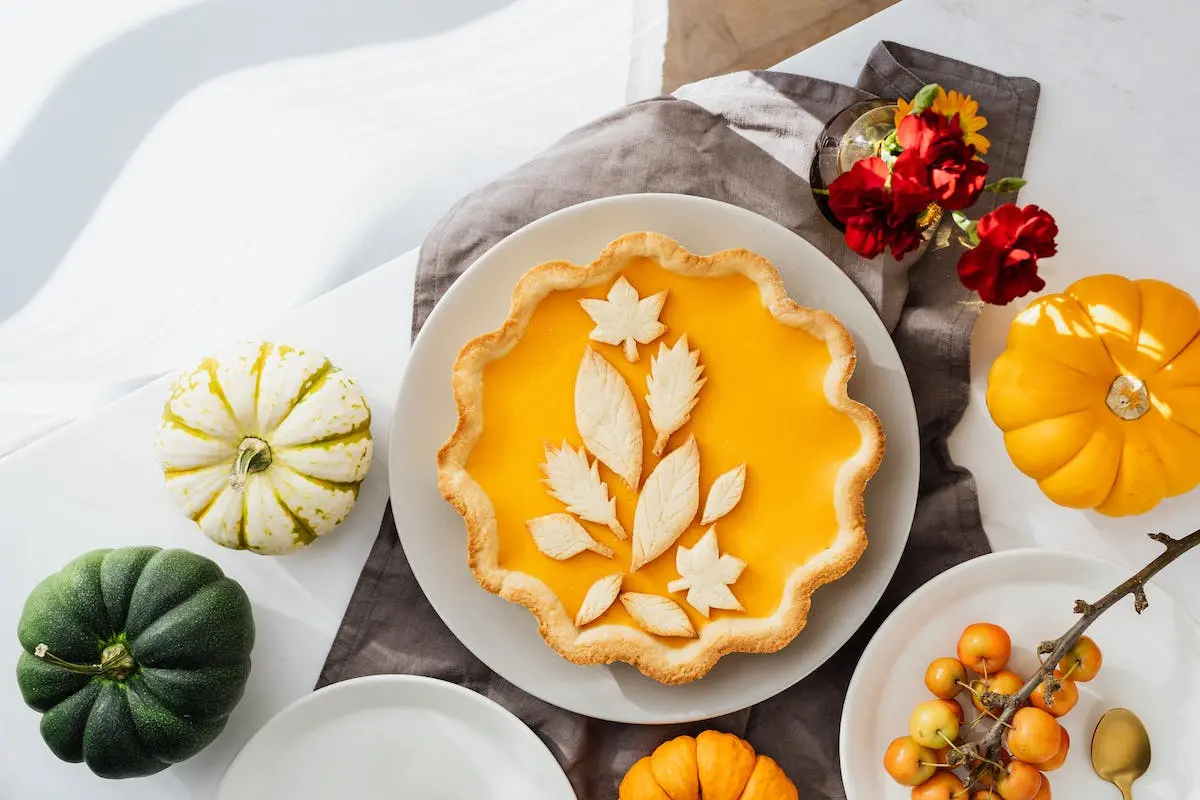A pumpkin custard pie with decorative pastry leaves, presented among fall decorations, epitomizing the warmth and charm of the season.