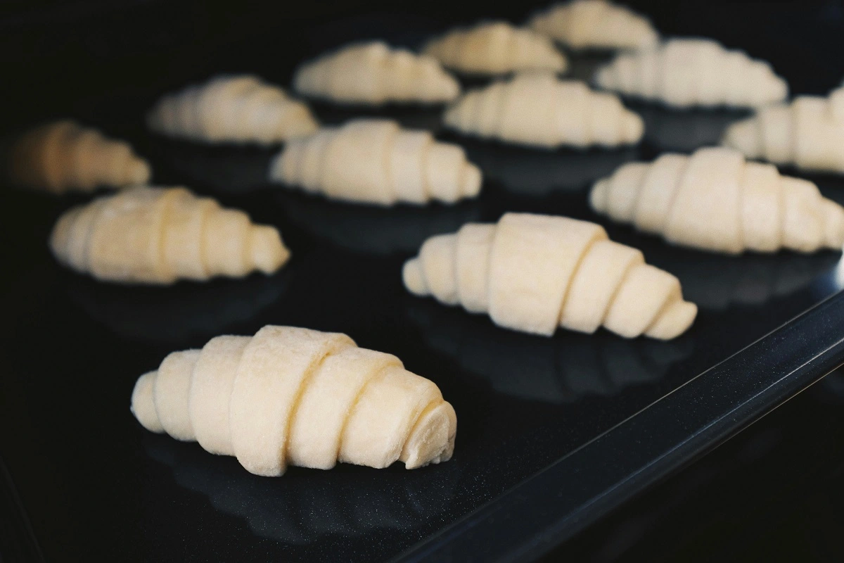 Unbaked mini croissant dough arranged on a baking tray, prepped for the oven to become flaky croissants.