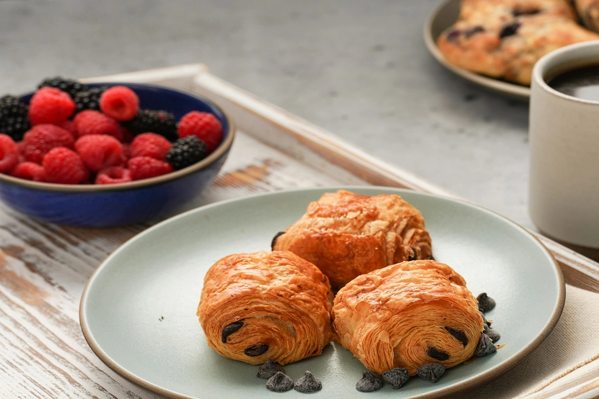 Two mini chocolate croissants on a plate with a side bowl of mixed berries, suggesting a tempting breakfast option.